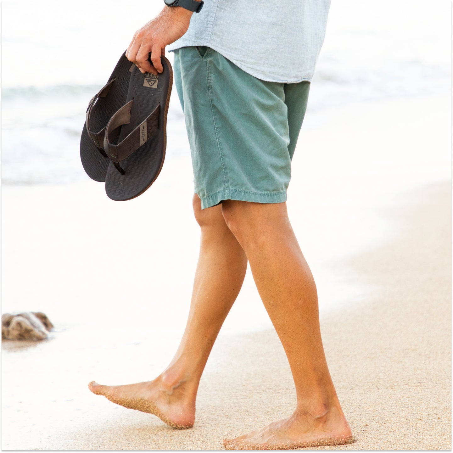 Man holding brown reef santa ana sandals on the beach Lifestyle